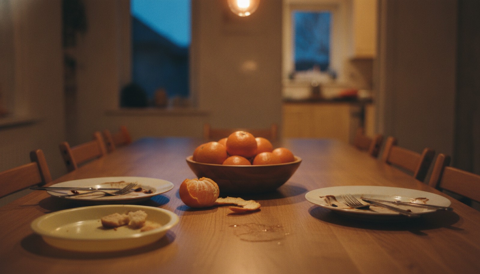 A dining table late in a meal with two dinner plates pushed back, a smaller child's plate to one side and a bowl of clementines in the middle