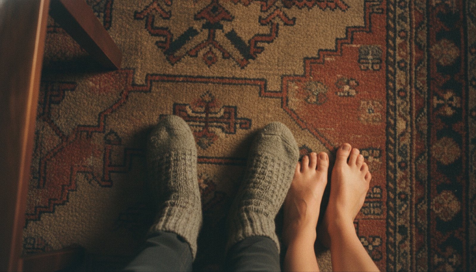 Two pairs of feet mid-turn on a living room rug with the coffee table pushed against the couch under one warm lamp
