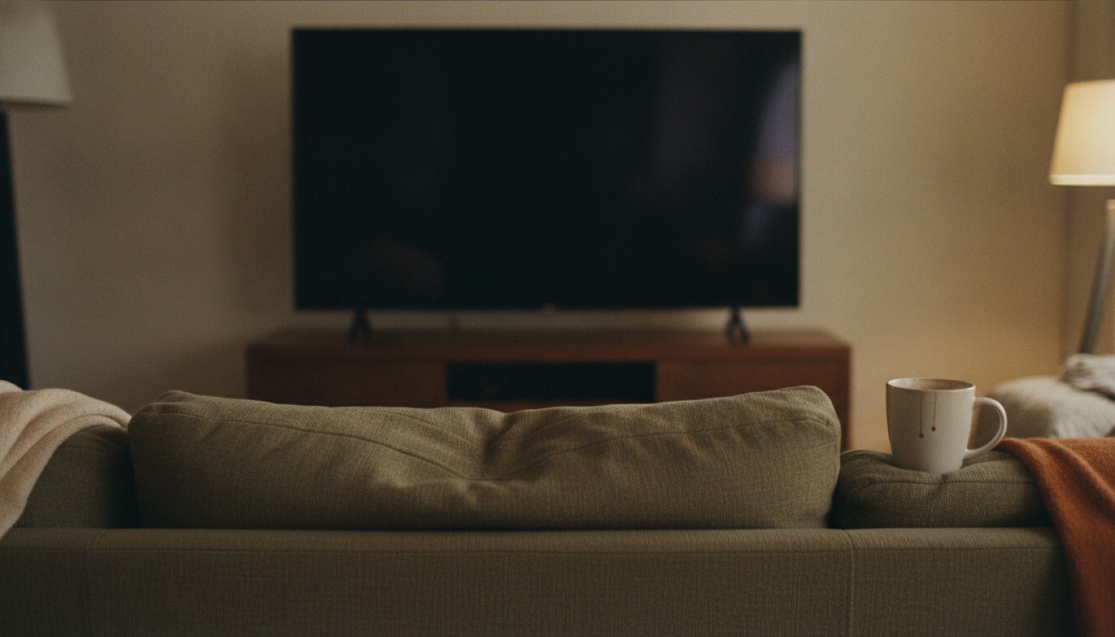 A sofa with one cushion dented and a television dark in front of it in evening light