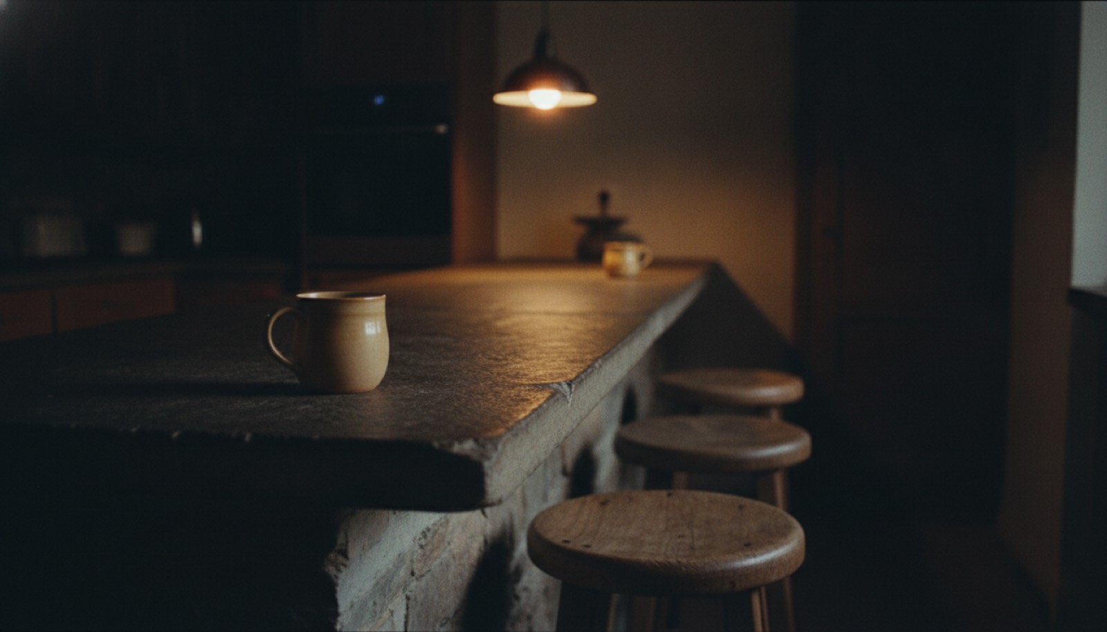 Two chairs at opposite ends of a long kitchen counter with a lamp lit between them at night