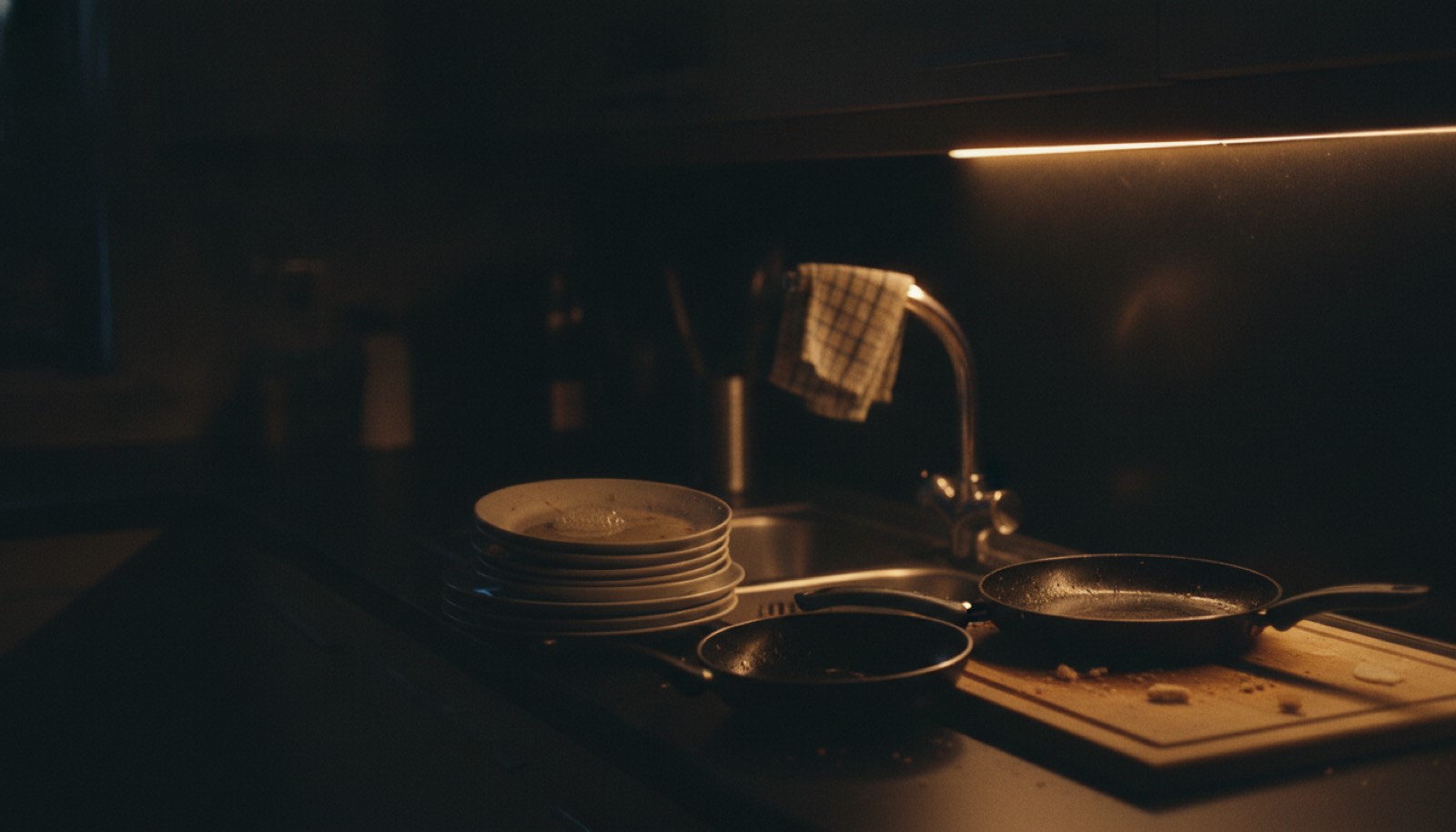 A kitchen at the end of the day with dishes stacked by the sink and one light left on