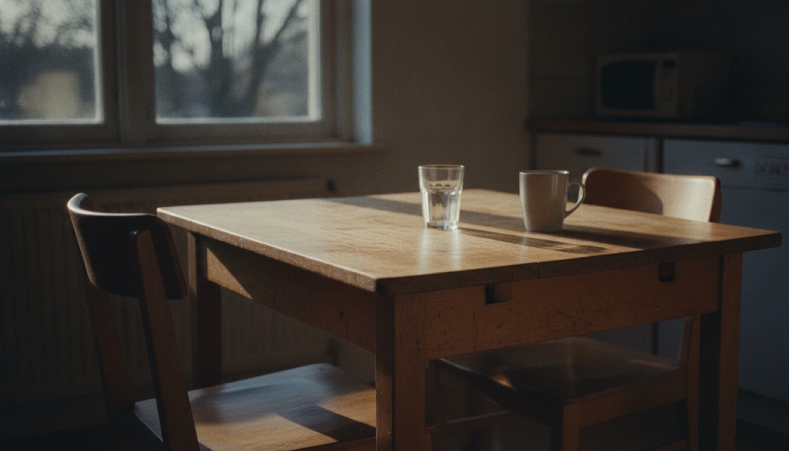 A wooden kitchen table with two chairs at right angles and a low winter sun across it