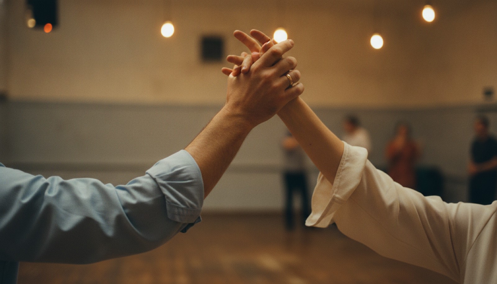 Two hands clasped and raised overhead in a swing turn, the arms cropped at the elbows, in a warmly lit community hall