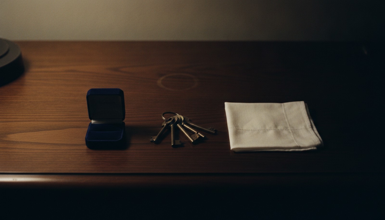 A ring box, a set of keys and a folded handkerchief laid out in a row on a dark wooden dresser