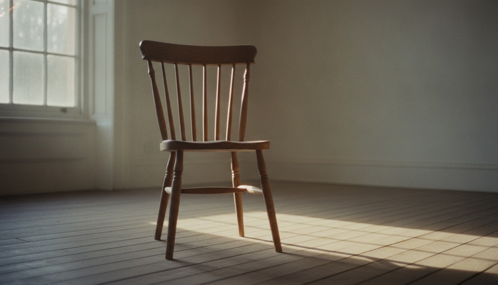 A single wooden chair by a window in an empty room with morning light across the floorboards